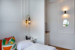 A bedroom with a bed, a nightstand, a mirror, and a wall-mounted light fixture.