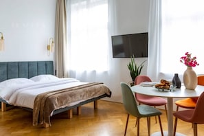 A bedroom with a bed, bedside table, TV, and a dining area with chairs and a table.