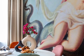 A room with a large painting, a vase with flowers, a plate with pastries, and a chair.