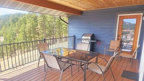 Eine überdachte Terrasse im Freien mit Grill, Glastisch und Stühlen.