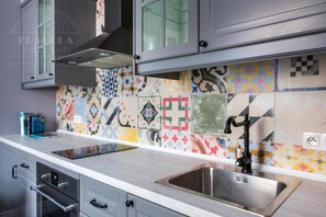 A kitchen with a stainless steel sink, a modern stove, and a colorful tile backsplash.
