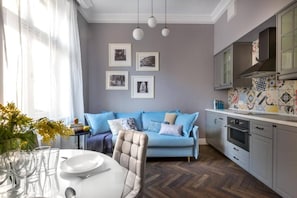 A modern kitchen with a herringbone floor, a blue sofa, and a dining table set with glasses and plates.