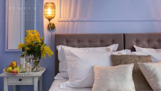 A bedroom with a bed, pillows, a bedside table with fruit and a vase of flowers, and a wall-mounted lamp. - Apartment Lavender - One Bedroom Apartment, Sleeps 4 (Kraków – Old Town)