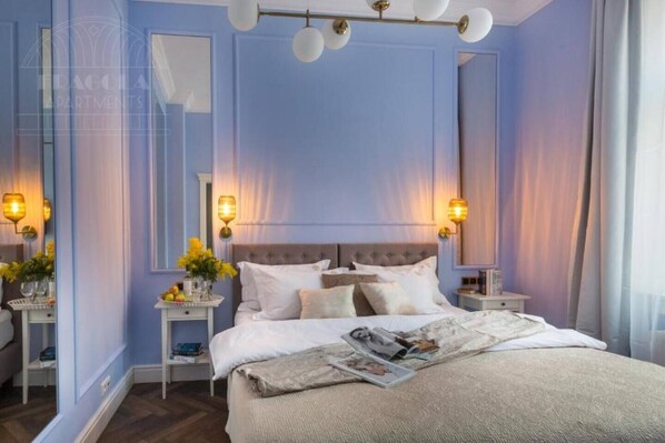 A bedroom with a large bed, bedside tables, a mirror, and wall sconces.