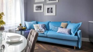 A room with a blue sofa, a dining table with plates and cutlery, and framed pictures on the wall. - Apartment Lavender - One Bedroom Apartment, Sleeps 4 (Kraków – Old Town)
