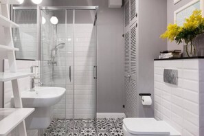 Un baño moderno con ducha de vidrio, un lavamanos blanco y un inodoro.