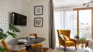 A modern living room with a round dining table, a sofa, and a TV mounted on the wall. - Sunny studio with balcony (Kraków – Old Town)