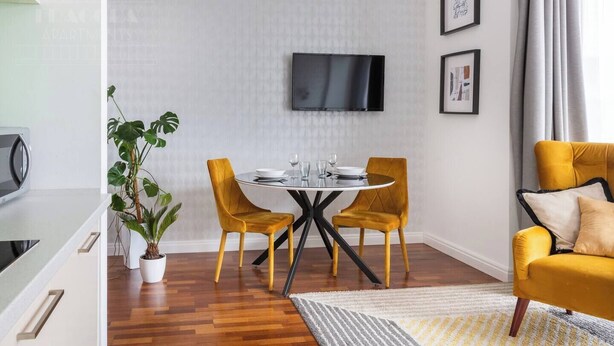 A modern living room with a round table, two yellow chairs, a sofa, a flat-screen TV, and a potted plant. - Sunny studio with balcony (Kraków – Old Town)