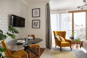 Een moderne woonkamer met een ronde eettafel, een bank en een aan de muur bevestigde televisie.