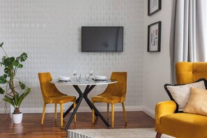 A dining area with a round table, two chairs, a television on the wall, and a yellow sofa. - Sunny studio with balcony (Kraków – Old Town)