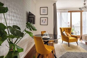 Uma sala de estar moderna com uma mesa de jantar redonda, cadeiras amarelas, uma planta grande e vista da cidade através de janelas amplas.