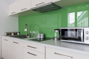 A kitchen with a green backsplash, a stainless steel microwave, a coffee maker, and a sink with a faucet. - Sunny studio with balcony (Kraków – Old Town)