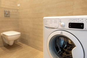 Um banheiro moderno com vaso sanitário branco e máquina de lavar INDESIT.