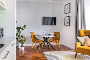 Un salon moderne avec une table ronde, deux fauteuils jaunes, un canapé, un téléviseur à écran plat et une plante en pot.