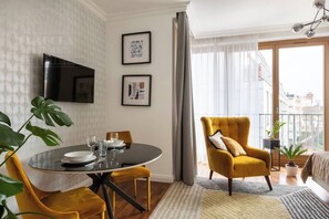 A modern living room with a round dining table, a sofa, and a TV mounted on the wall. - Sunny studio with balcony (Kraków – Old Town)