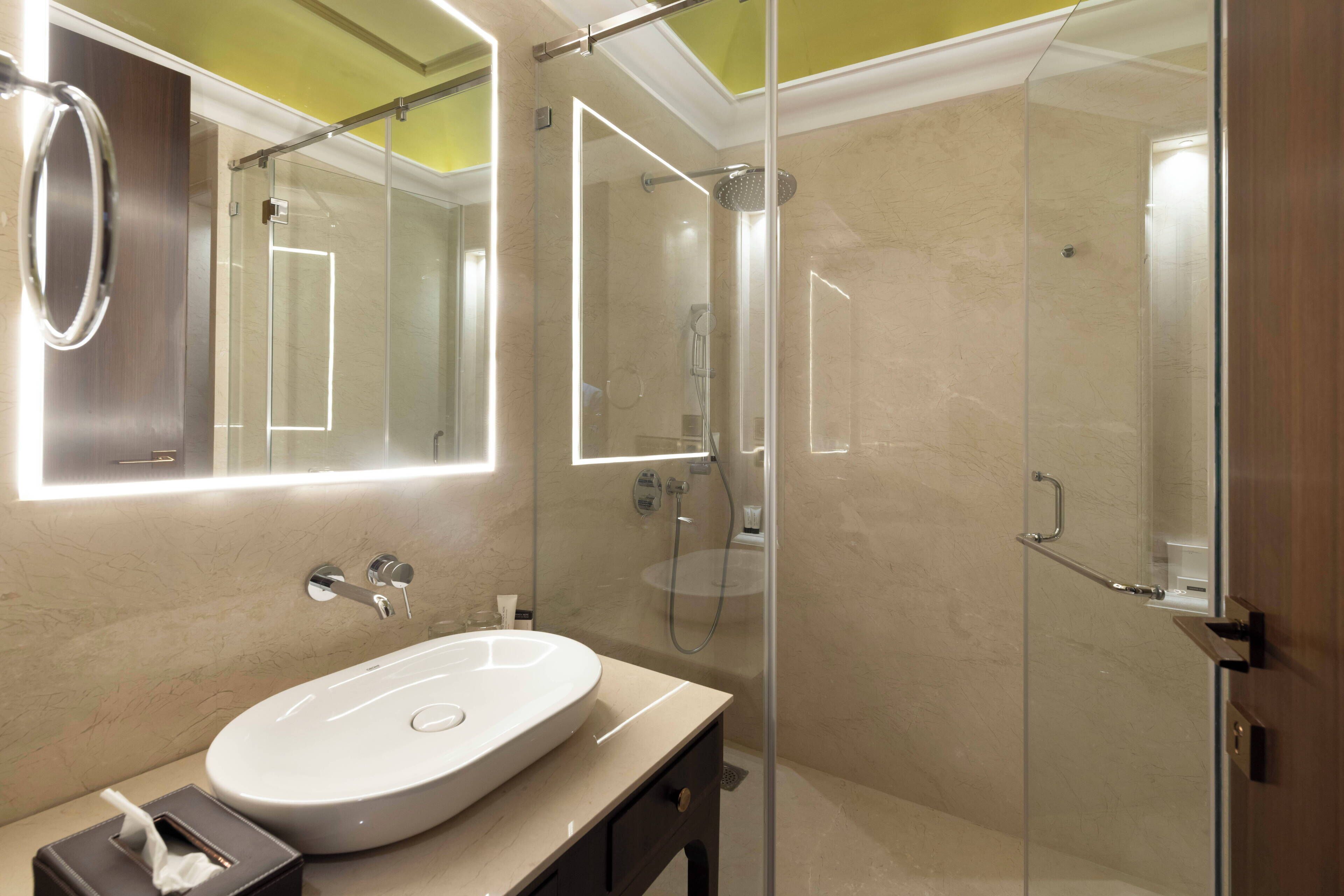 Un baño moderno con un espejo grande, ducha con cerramiento de vidrio y tocador color crema.