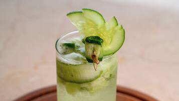Un vaso alto con una bebida verde, adornado con rodajas de pepino y hojas de menta, sobre una bandeja de madera.