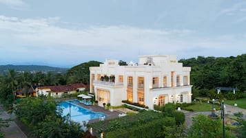 A large, white building with a pool and lush greenery.