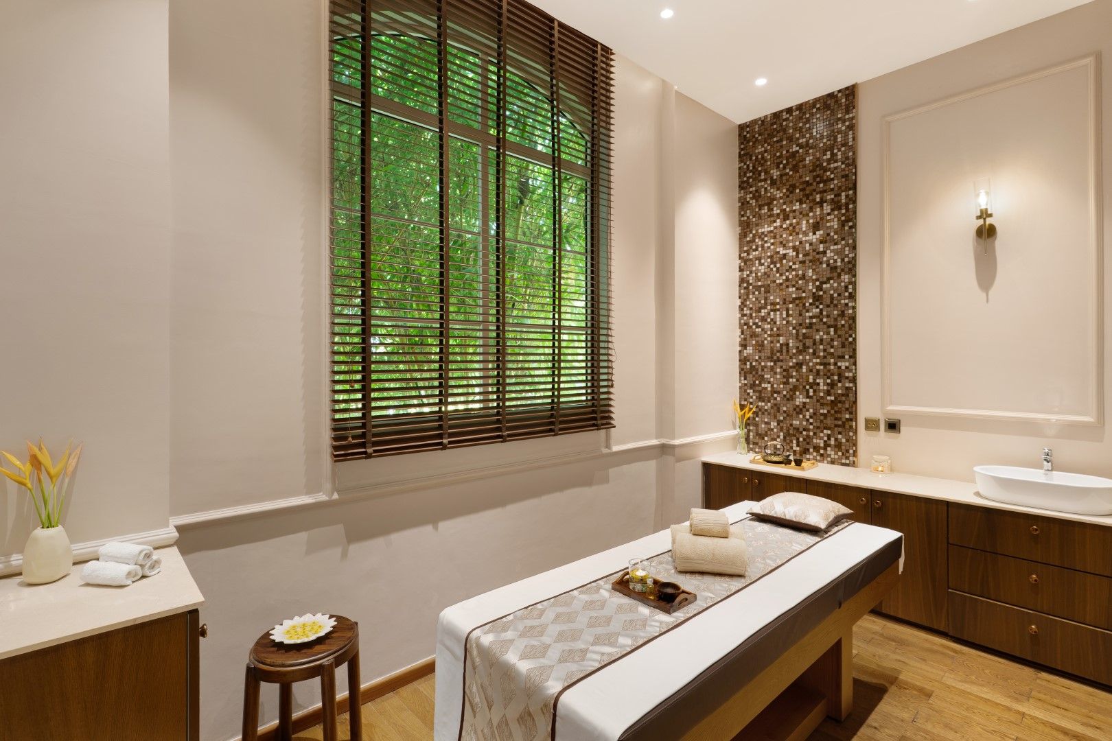 A spa room with a massage table, a wooden cabinet, a sink, and a window with blinds.
