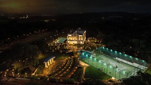 Un grand bâtiment illuminé, doté d’une piscine et de courts de tennis.
