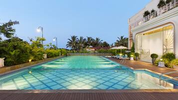 A swimming pool with a tiled pattern, surrounded by a wooden deck and palm trees.