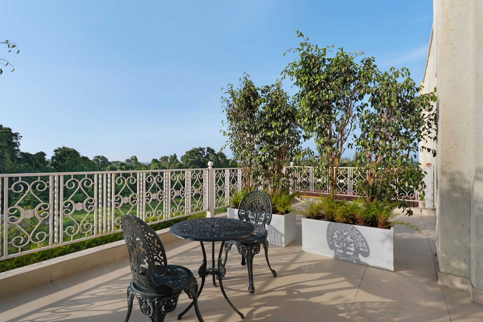 An outdoor patio with two metal chairs and a table, surrounded by a decorative fence and lush greenery.