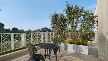 An outdoor patio with two metal chairs and a table, surrounded by a decorative fence and lush greenery.