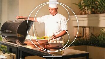 A chef in a white uniform preparing food at a table with a grill and bowls of food.