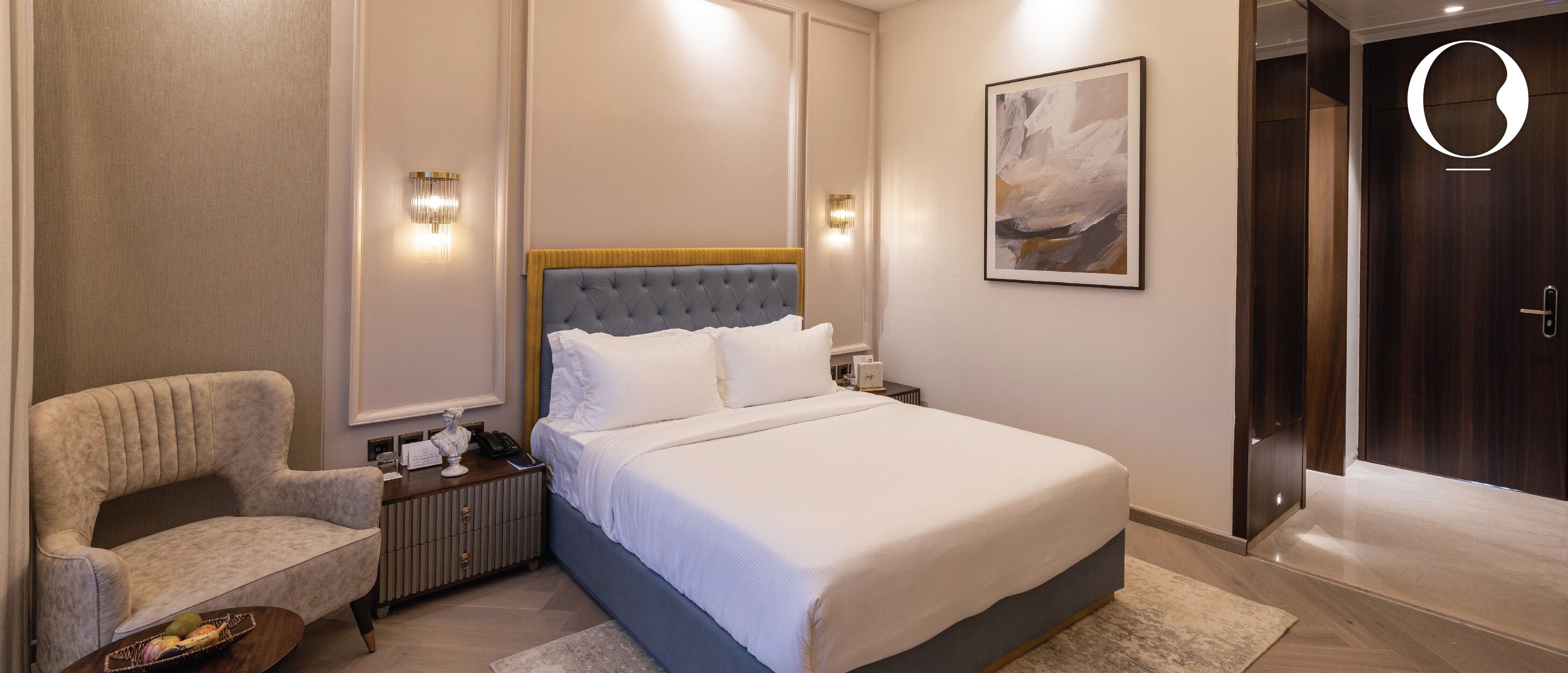 A hotel room with a large bed, a nightstand, a chair, and a door.