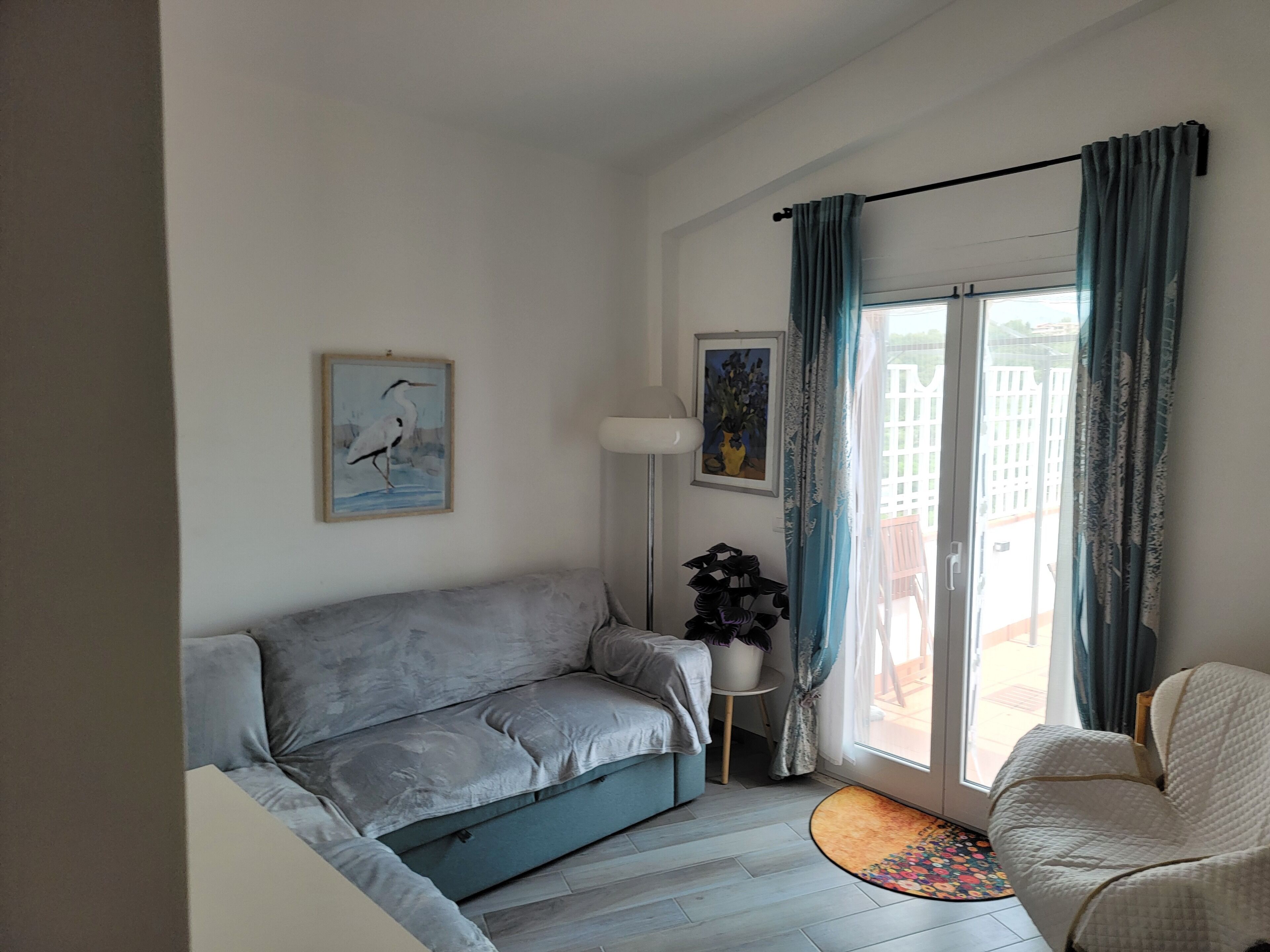 A living room with a grey sofa, a white armchair, a floor lamp, and a door leading to an outdoor area.