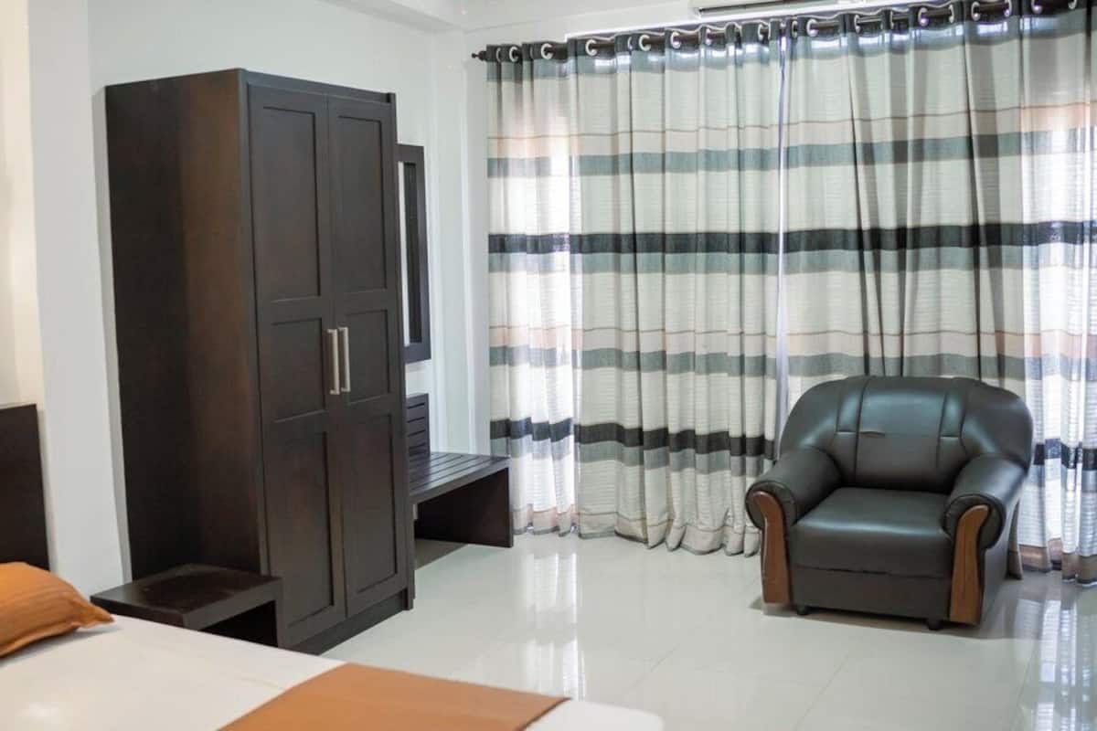 A bedroom with a bed, a dark wooden wardrobe, a leather armchair, and striped curtains.