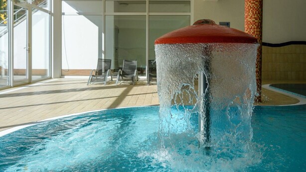 A pool with a water feature, indoor seating area, and large windows. - Chickes Appartement (Mirow)