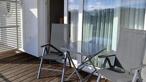A balcony with a glass table and two chairs, a sliding glass door, and a white exterior wall. - Chickes Appartement (Mirow)
