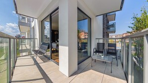 A modern balcony with glass doors, a dining area with chairs and a table, and a view of the cityscape. - Apartament Sun & Snow Kaszubska Bryza ll (Hel)