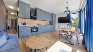 A modern kitchen with grey cabinets, a wooden dining table, and a built-in oven. - Apartament Sun & Snow Kaszubska Bryza ll (Hel)