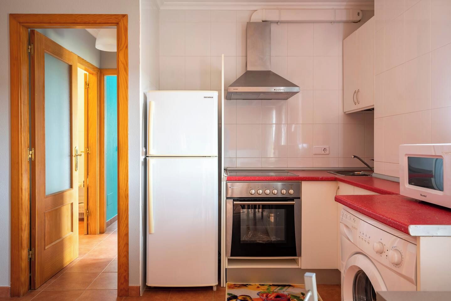 A kitchen with a refrigerator, oven, microwave, and washing machine.