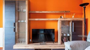 A modern living room with a television, wooden furniture, and orange walls. - Apartamento Ruiloba-Comillas (Ruilobuca)