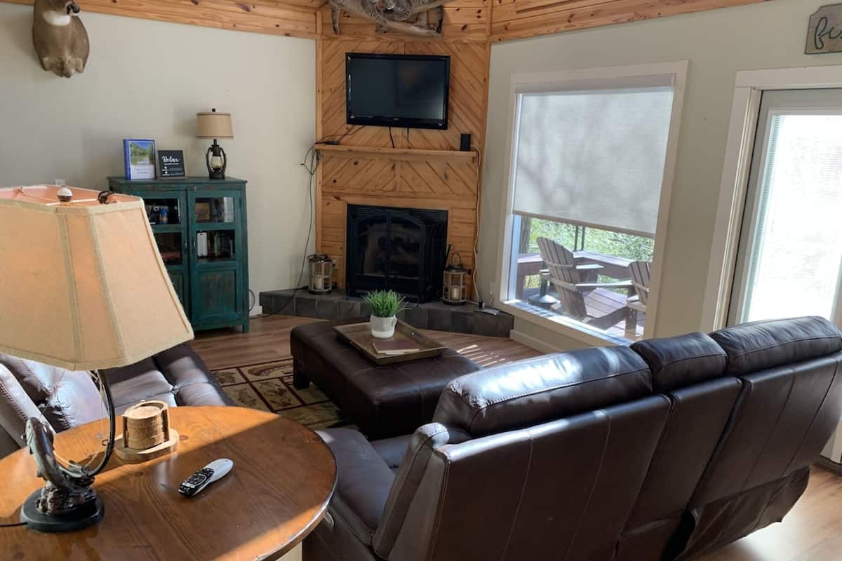 Un intérieur de chalet chaleureux avec une cheminée, un canapé en cuir, des murs en bois et un téléviseur.