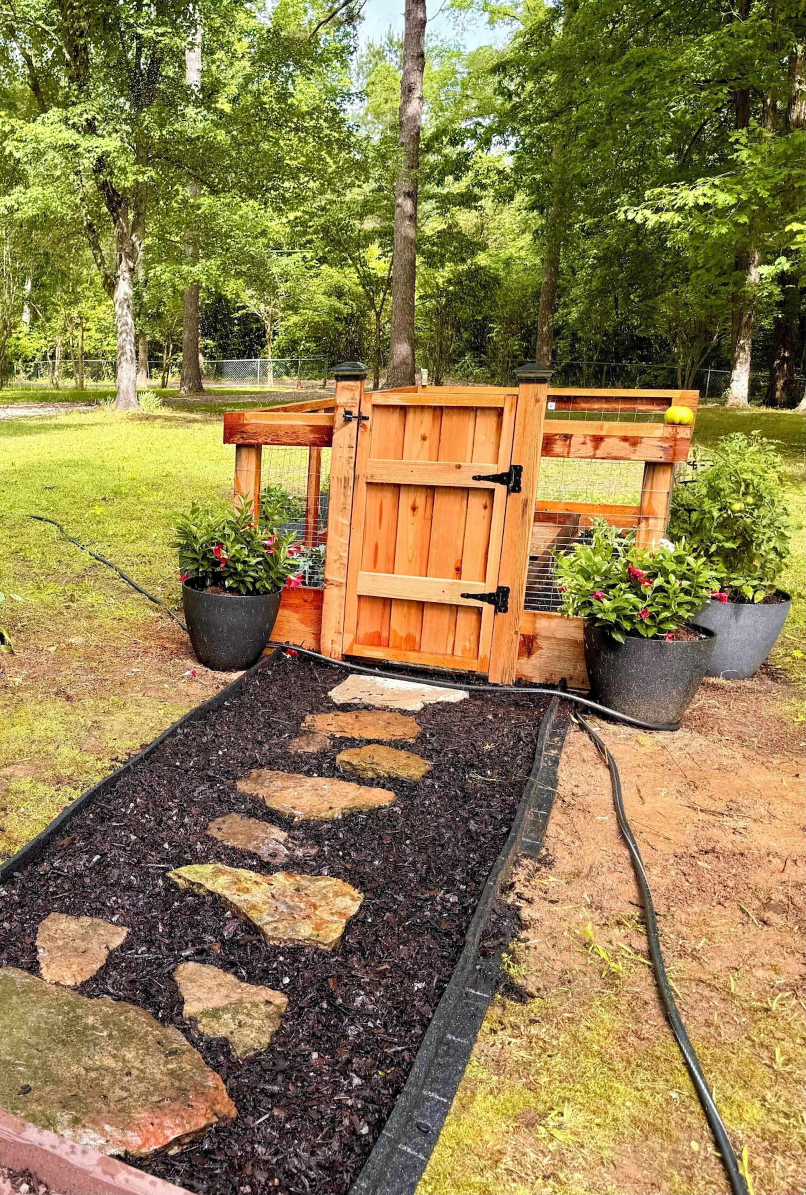 A wooden gate leading to a garden area with potted plants and a stone pathway.