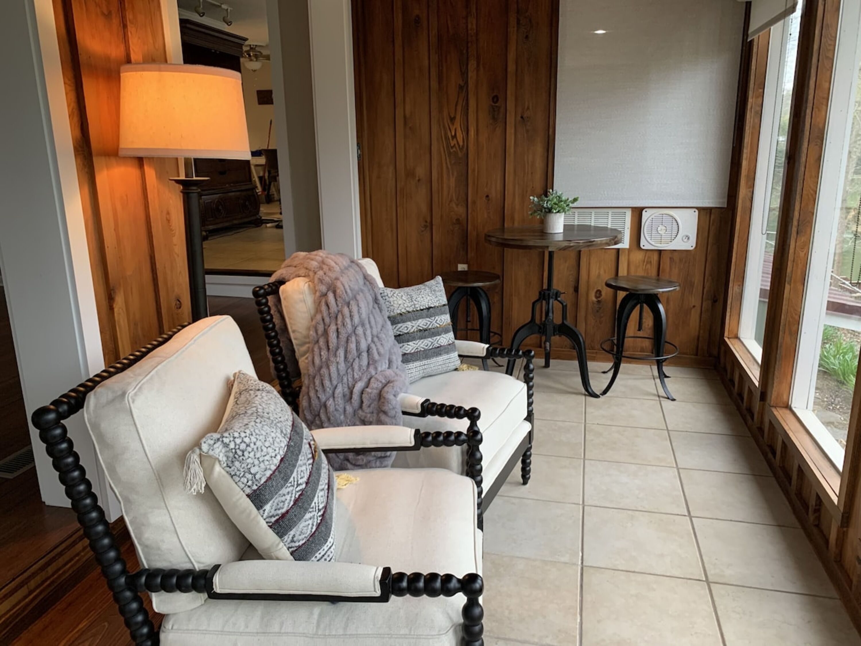A cozy seating area with a cushioned chair and a table, wooden walls, and a window providing a view.