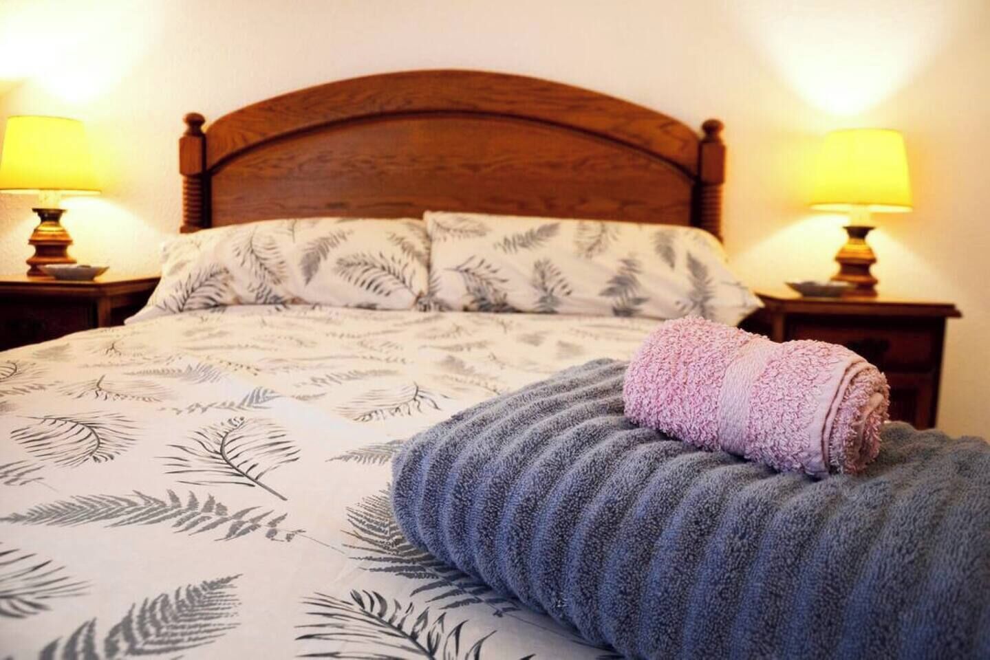 A bed with a patterned bedspread, a rolled towel, and two bedside lamps.