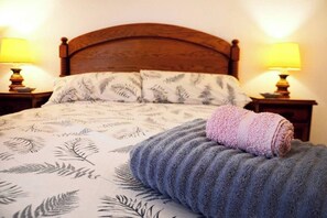 A bed with a patterned bedspread, a rolled towel, and two bedside lamps. - Apartamento en Somo con 2 plazas de garaje (Somo)