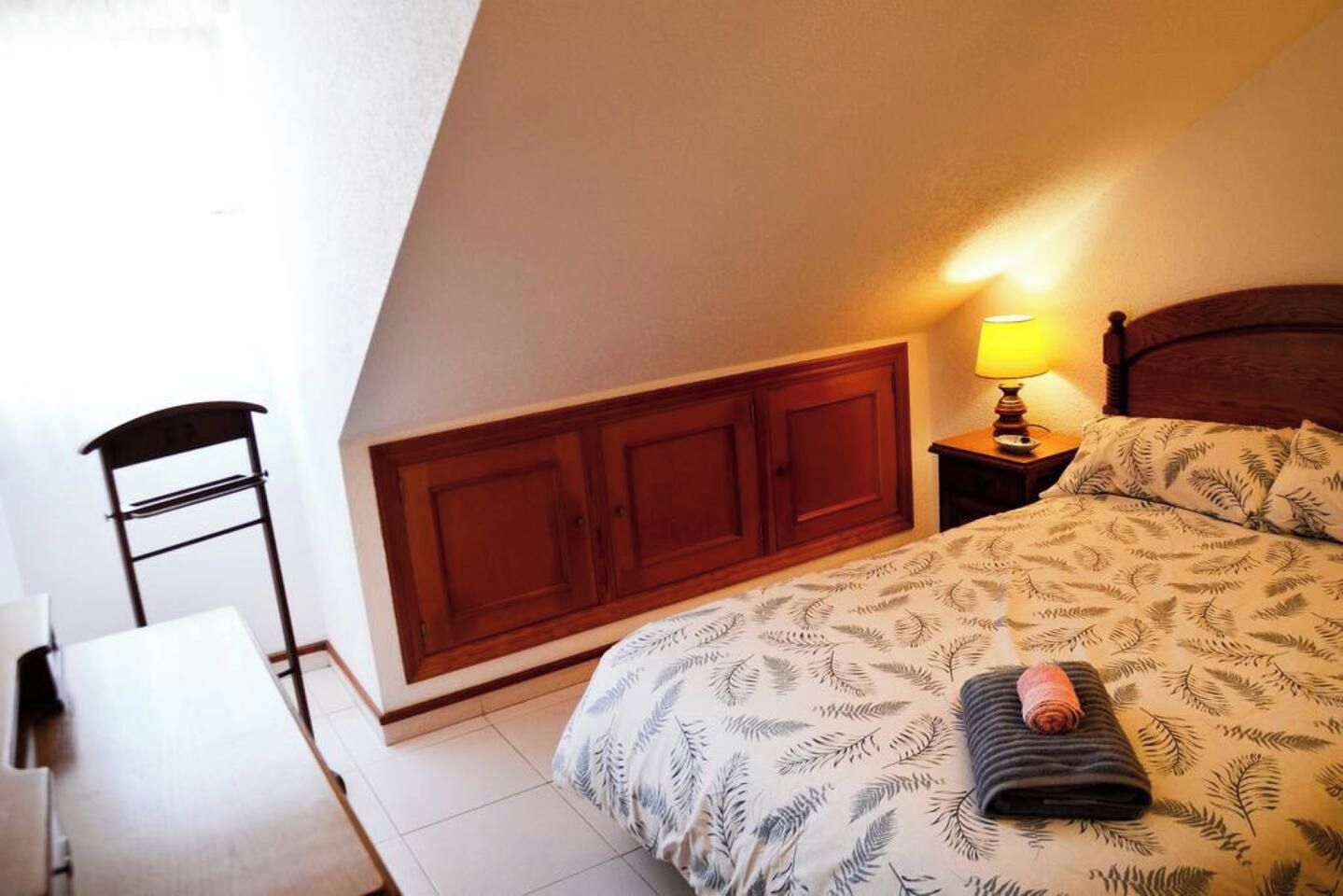 A bedroom with a bed, a nightstand, a lamp, a chair, and a wardrobe.