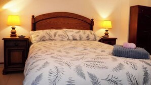 A bed with a leaf-patterned bedspread, two bedside lamps, a wooden headboard, and a nightstand with a drawer. - Apartamento en Somo con 2 plazas de garaje (Somo)