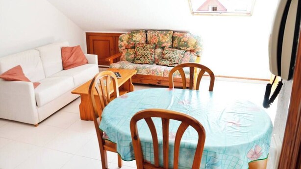 A living room with a white sofa, a floral sofa, a dining table with chairs, and a small window. - Apartamento en Somo con 2 plazas de garaje (Somo)