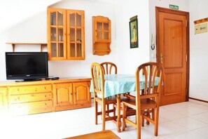Un comedor con una mesa lista para dos personas, armarios de madera, un televisor y una puerta con la etiqueta 'SALIDA'.