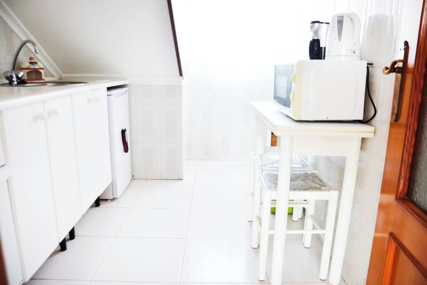 Una cucina con mobili bianchi, un tavolino e un forno a microonde.