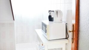 A white microwave on a small white table in a room with white walls and a wooden door. - Apartamento en Somo con 2 plazas de garaje (Somo)