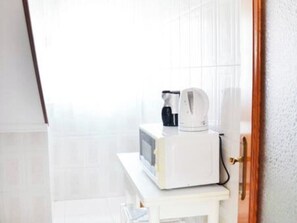 Un microondas blanco sobre una pequeña mesa blanca en una habitación con paredes blancas y una puerta de madera.