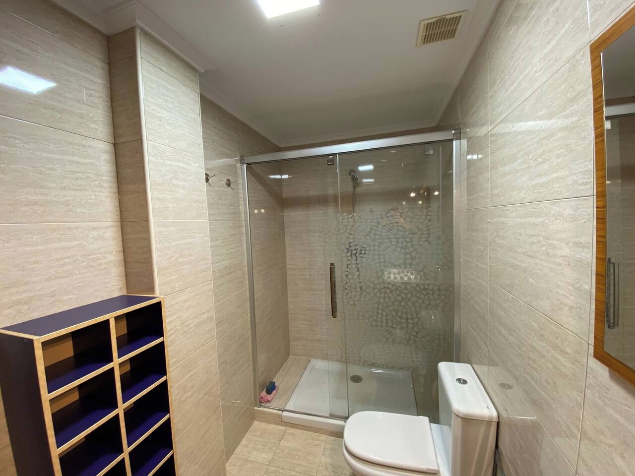 Un baño moderno con ducha de vidrio, inodoro y estantería empotrada.